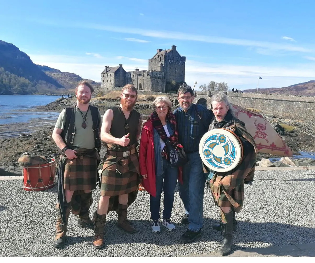 A family with kilted pipers in front of Eilean Donan Castle